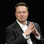 Man in suit clasping hands against black background