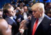 A man in a suit speaking passionately surrounded by cameras and reporters