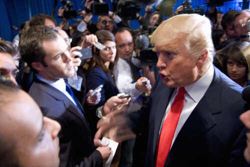 A man in a suit speaking passionately surrounded by cameras and reporters