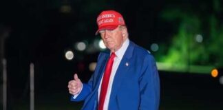 A man in a blue suit and red cap giving a thumbs up at night