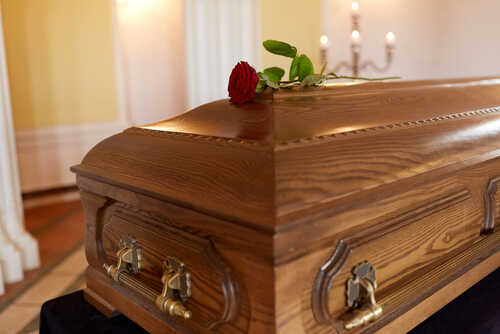 shutterstock_741689236.jpg A wooden casket with a red rose on top, set in a softly lit room