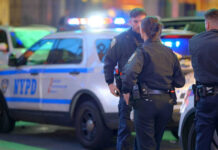 Police officers standing near NYPD vehicles at night