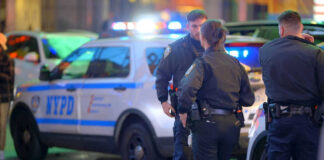 Police officers standing near NYPD vehicles at night
