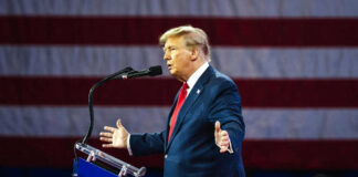 Man speaking at podium with American flag background