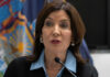Woman speaking at a podium with flags behind
