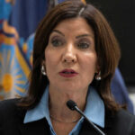 Woman speaking at a podium with flags behind