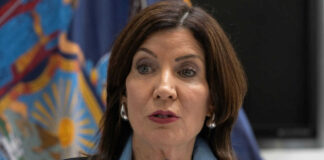 Woman speaking at a podium with flags behind