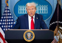 Person speaking at a podium with flags behind