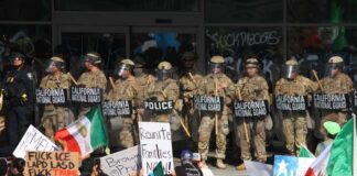 Protesters holding signs and flags in front of a line of National Guard members