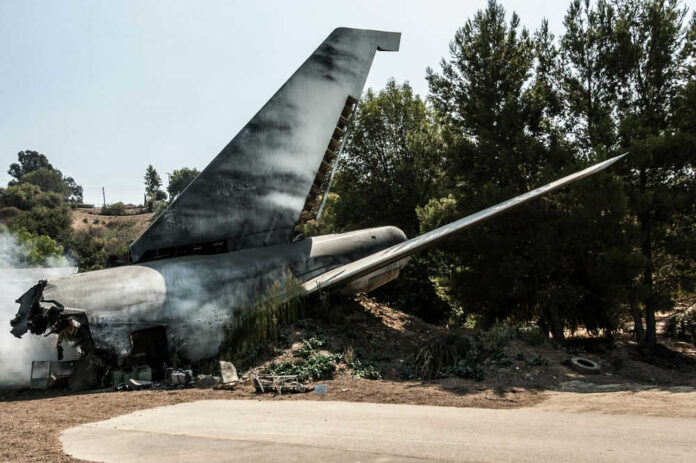 Plane wreckage in wooded area with smoke rising