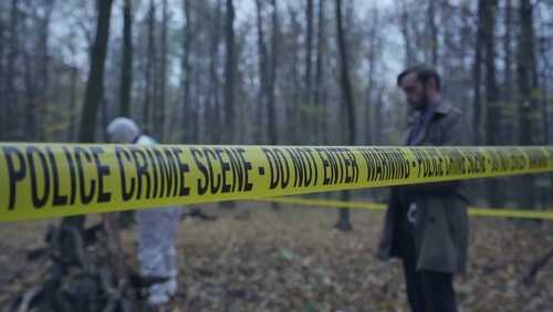 Police crime scene tape in a forest with investigators