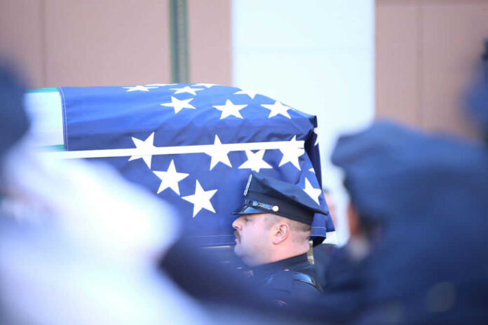 shutterstock_240275638 Officer standing beside flagdraped casket at ceremony