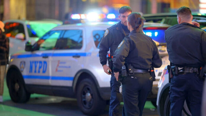 Police officers standing near NYPD vehicles at night