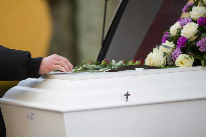 Hand resting on coffin adorned with flowers