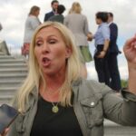 A woman passionately speaking outdoors, surrounded by people and media.