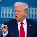 A man in a suit speaking at a press conference with a serious expression