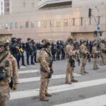 Line of law enforcement officers in tactical gear standing on a city street