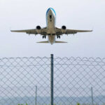 Airplane taking off above a wire fence