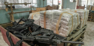 Pallets of wrapped packages beside a crate of firearms