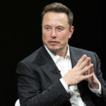 Man in black suit sitting with hands clasped