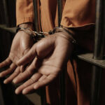 Person handcuffed behind prison bars in orange jumpsuit