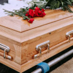 Wooden coffin with red roses and green leaves