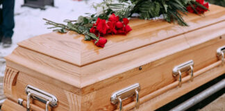 Wooden coffin with red roses and green leaves