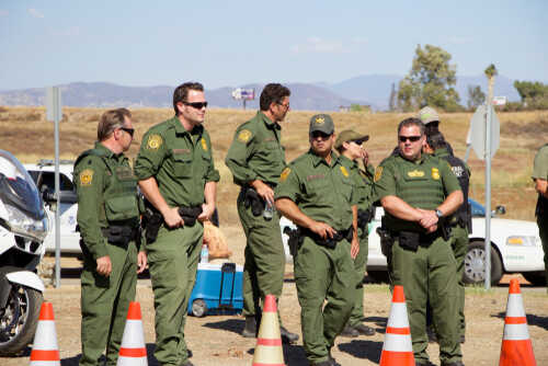 Group of law enforcement officers in green uniforms standing near traffic cones